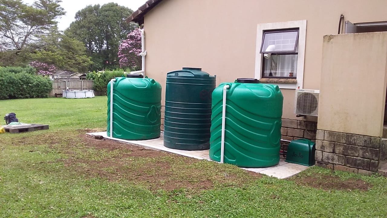 Three green water tanks and connected pipework beside the house at the Crestholme installation.
